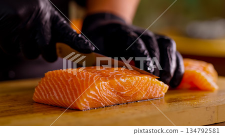 A person cutting up a piece of salmon on a cutting board with a knife 134792581