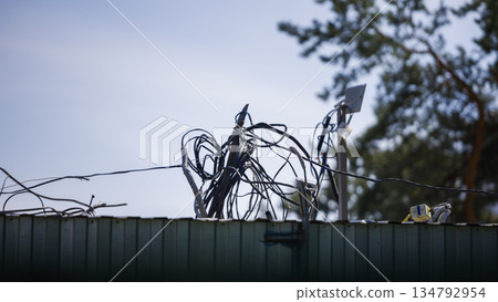 Cables and wires are tangled on a structure with a tree line in the background under a clear sky during daylight 134792954