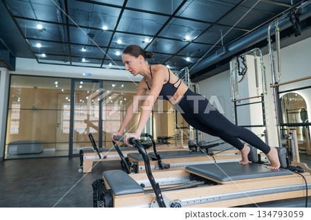 Caucasian woman doing exercises on reformer machine. Caucasian woman doing exercises on reformer machine. 134793059