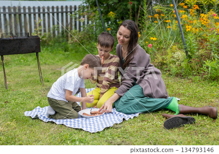 Caucasian woman eats fried sausages with her sons at a picnic. Caucasian woman eats fried sausages with her sons at a picnic. 134793146