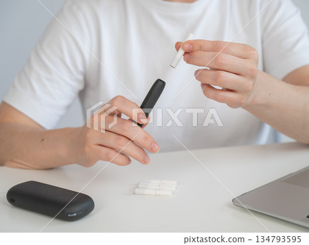 A woman inserts a cigarette stick into a tobacco heating system. Electronic cigarette. 134793595
