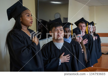 Graduates stand proudly at the ceremony with their hands over their hearts. Graduates stand proudly at the ceremony with their hands over their hearts. 134793603