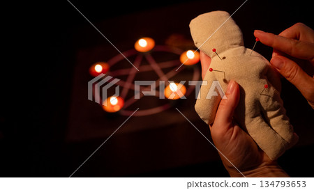 Woman sticking pins into voodoo doll. Woman sticking pins into voodoo doll. 134793653