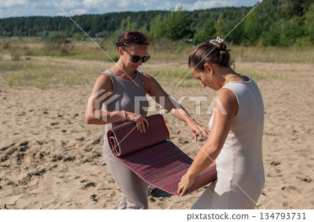 Two Caucasian women spread a blanket on the beach for a picnic.  134793731
