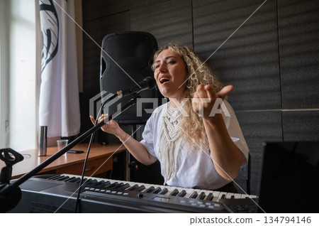 Caucasian woman singing into microphone and playing synthesizer and recording herself on laptop.  134794146