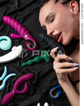 Portrait of Caucasian woman lying on bed among sex toys. Portrait of Caucasian woman lying on bed among sex toys. 134794160