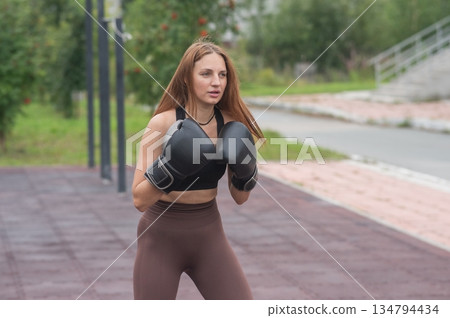 A Caucasian woman practices boxing outdoors.  134794434