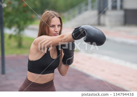 A Caucasian woman practices boxing outdoors.  134794438