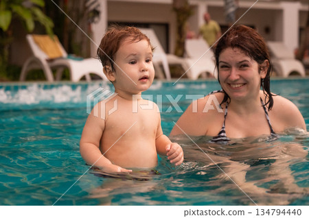 Caucasian woman holds her son while swimming in a pool on vacation. Mom teaches little boy to swim. Caucasian woman holds her son while swimming in a pool on vacation. Mom teaches little boy to swim. 134794440