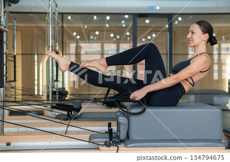 Caucasian woman doing exercises on reformer machine. Caucasian woman doing exercises on reformer machine. 134794675