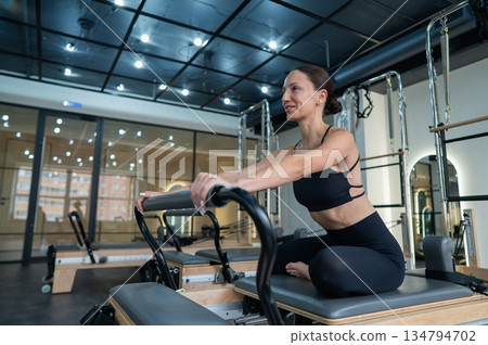 Caucasian woman doing exercises on reformer machine. Caucasian woman doing exercises on reformer machine. 134794702