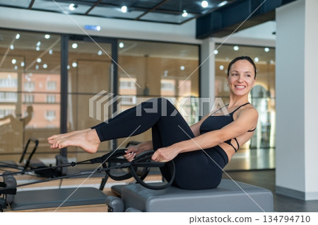 Caucasian woman doing exercises on reformer machine. Caucasian woman doing exercises on reformer machine. 134794710
