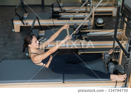 Caucasian woman doing exercises on reformer machine. Caucasian woman doing exercises on reformer machine. 134794730