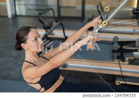 Caucasian woman doing exercises on reformer machine. Caucasian woman doing exercises on reformer machine. 134794733