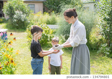 Caucasian woman tending her garden with her sons. Caucasian woman tending her garden with her sons. 134794801