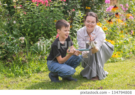 Caucasian woman tending her garden with her son. Caucasian woman tending her garden with her son. 134794808