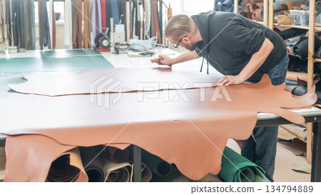 Caucasian bearded man working as a tanner in a workshop. Caucasian bearded man working as a tanner in a workshop. 134794889