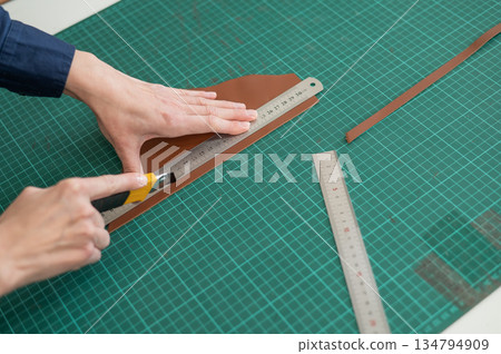 Leatherworker measuring and cutting leather in workshop. Leatherworker measuring and cutting leather in workshop. 134794909