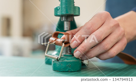A woman attaches accessories to a leather belt. Leatherworker's workshop.  134794913
