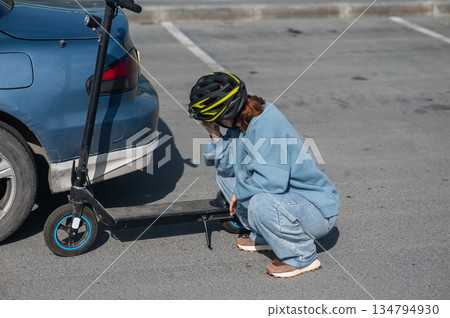 A distressed woman examines the damage after a collision between an electric scooter and a car. A distressed woman examines the damage after a collision between an electric scooter and a car. 134794930