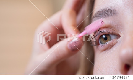 Caucasian woman brushing her eyelashes after lamination. Caucasian woman brushing her eyelashes after lamination. 134794935