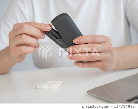 A woman smokes an electronic cigarette while working on a laptop. Tobacco heating system. A woman smokes an electronic cigarette while working on a laptop. Tobacco heating system. 134794986