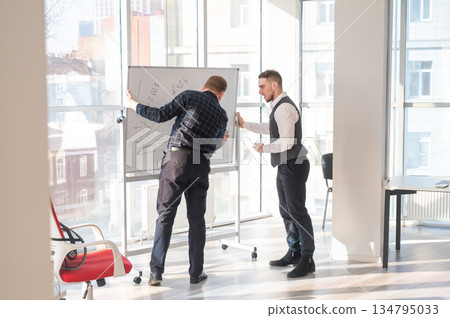 Two Caucasian men discussing work at a white board. Two Caucasian men discussing work at a white board. 134795033
