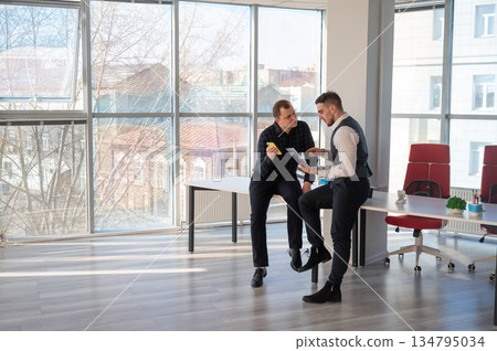 Two Caucasian men discussing work in an office. Businessman with a hearing aid. Two Caucasian men discussing work in an office. Businessman with a hearing aid. 134795034