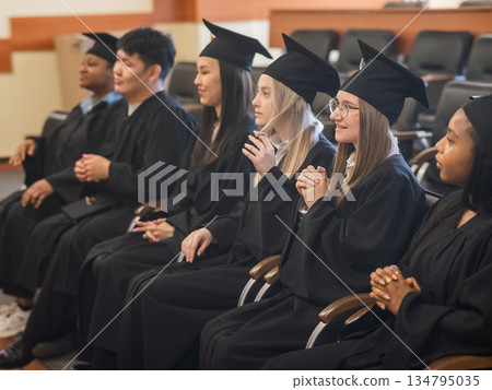 Graduates sit on a bench, listen to the speech and applaud. Graduates sit on a bench, listen to the speech and applaud. 134795035