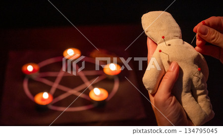 Woman sticking pins into voodoo doll. Woman sticking pins into voodoo doll. 134795045