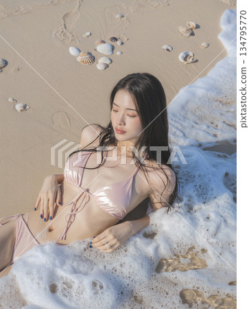Woman is laying on the beach in a bikini, with her hair wet 134795770