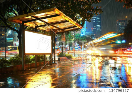 Nighttime City Bus Stop with Blank Digital Advert on Wet Pavement and Glowing Lights Nighttime City Bus Stop with Blank Digital Advert on Wet Pavement and Glowing Lights 134796527