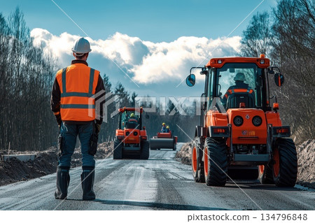 Construction Worker in Orange Vest Overseeing Road Work with Machinery in Background 134796848