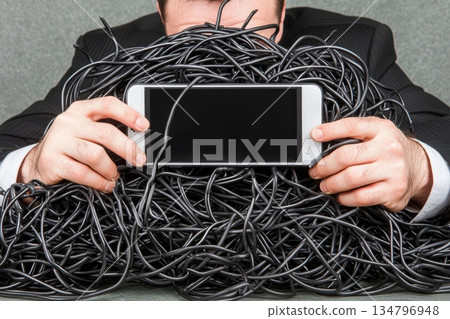 Person Holding Smartphone Surrounded by Tangle of Wires and Cables Like Lifeline 134796948