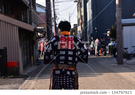 日本愛知縣犬山市：一名男子身穿法被，正在參加春季犬山祭，他正走在犬山城附近居民區的一條小巷裡。 134797923