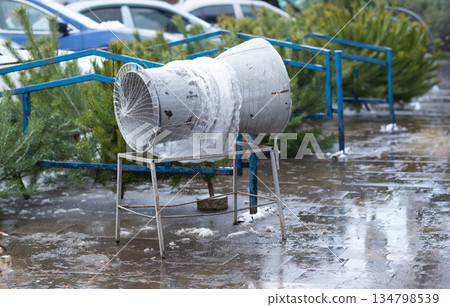 Manual Christmas tree netting funnel on a wet city sidewalk during a winter holiday market. 134798539