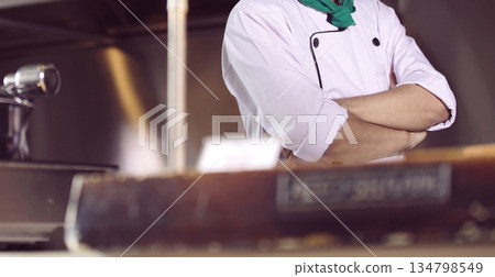 professional chef stands and working in a modern kitchen, wearing a white uniform. This image conveys expertise, focus, and readiness in a high demand culinary environment for restaurant profile 134798549