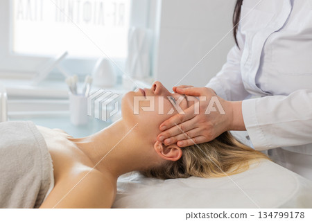 Woman having relaxing forehead massage procedure by professional beautician in cosmetology clinic Woman having relaxing forehead massage procedure by professional beautician in cosmetology clinic 134799178