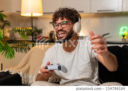 Arabian man plays video game on console holds joystick enjoys action excitement at night indoors fun 134799184