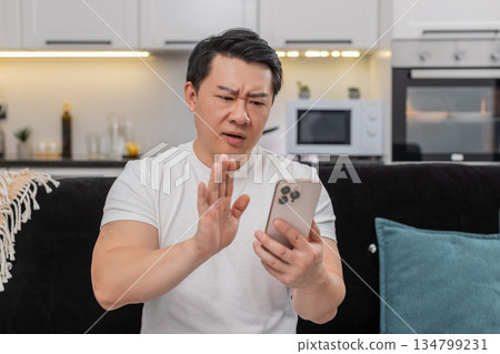 Asian man gets bad alert on smartphone frowns asks why shakes head no shows stop sign deletes mail Asian man gets bad alert on smartphone frowns asks why shakes head no shows stop sign deletes mail 134799231