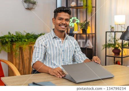 Indian man closes laptop with happy smile end of work day tasks done feels relief calm satisfaction Indian man closes laptop with happy smile end of work day tasks done feels relief calm satisfaction 134799234
