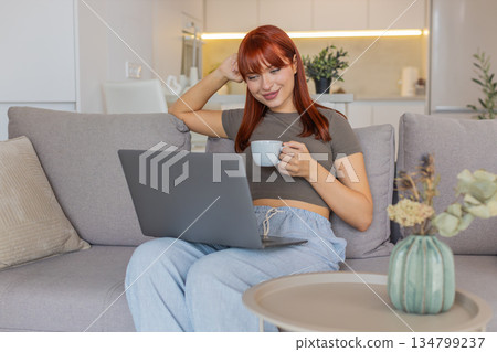 Young woman with coffee cup checks email on laptop works freelance remote tasks client inbox replies 134799237