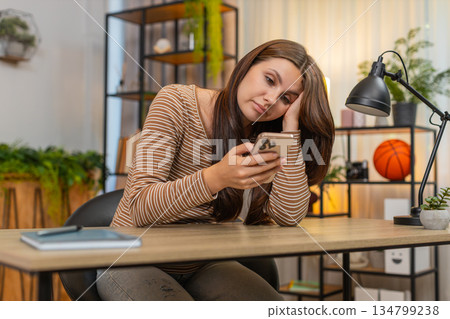 Young woman scrolls smartphone news feed bored unhappy drained by dull repetitive social media posts Young woman scrolls smartphone news feed bored unhappy drained by dull repetitive social media posts 134799238