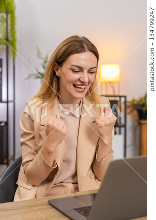 Businesswoman gets project approval message on laptop good news celebrates success victory gesture 134799247