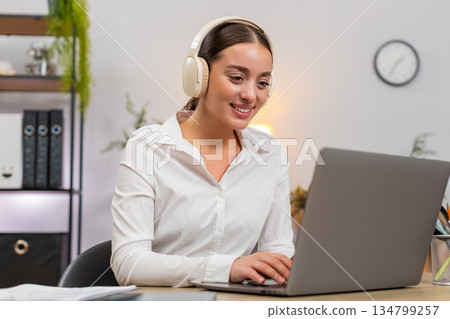 Young businesswoman in wireless headphones types on laptop hums to music and makes small dance move 134799257