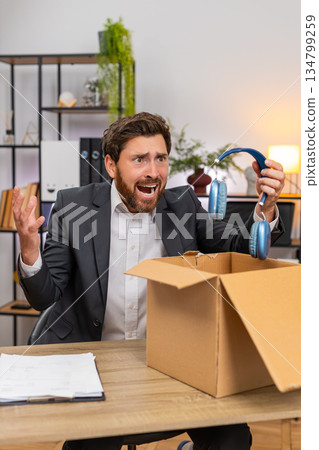 Middle-aged businessman unboxes delivery finds broken headphones looks disappointed requests return 134799259
