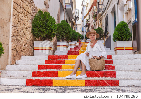 Young woman in a white dress sitting on the colourful Spanish Steps in the old town of Calpe, Spain, a well-known landmark painted in red and yellow Young woman in a white dress sitting on the colourful Spanish Steps in the old town of Calpe, Spain, a well-known landmark painted in red and yellow 134799269