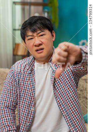 Asian man showing thumbs down, unhappy dislike expression signaling strong negative disagreement Asian man showing thumbs down, unhappy dislike expression signaling strong negative disagreement 134799314