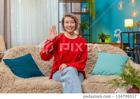 Young woman happily waving hand hello gesture friendly cheerful greeting expression smiling joyfully Young woman happily waving hand hello gesture friendly cheerful greeting expression smiling joyfully 134799317