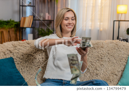 Woman throwing money dollar cash bills in air at home, celebrating lottery win with joy excitement 134799479